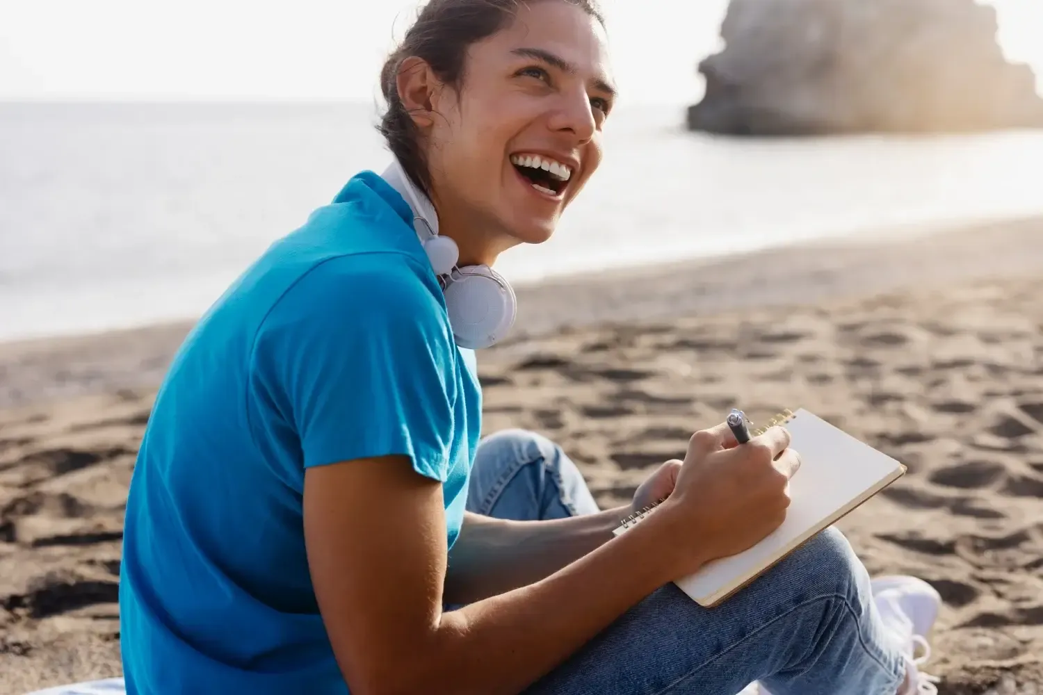 smiling person with journal sitting on the beach after retreat