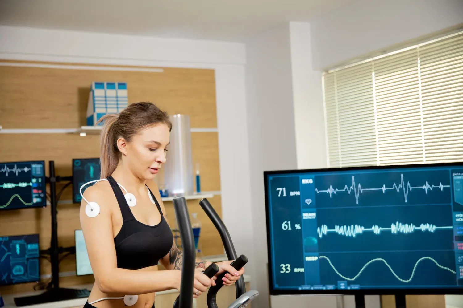 patient walking on a treadmill with electrodes attached, undergoing a stress test with heart monitoring in a clinical setting